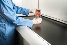 lab worker pouring liquid into container at safe distance from fume hood.